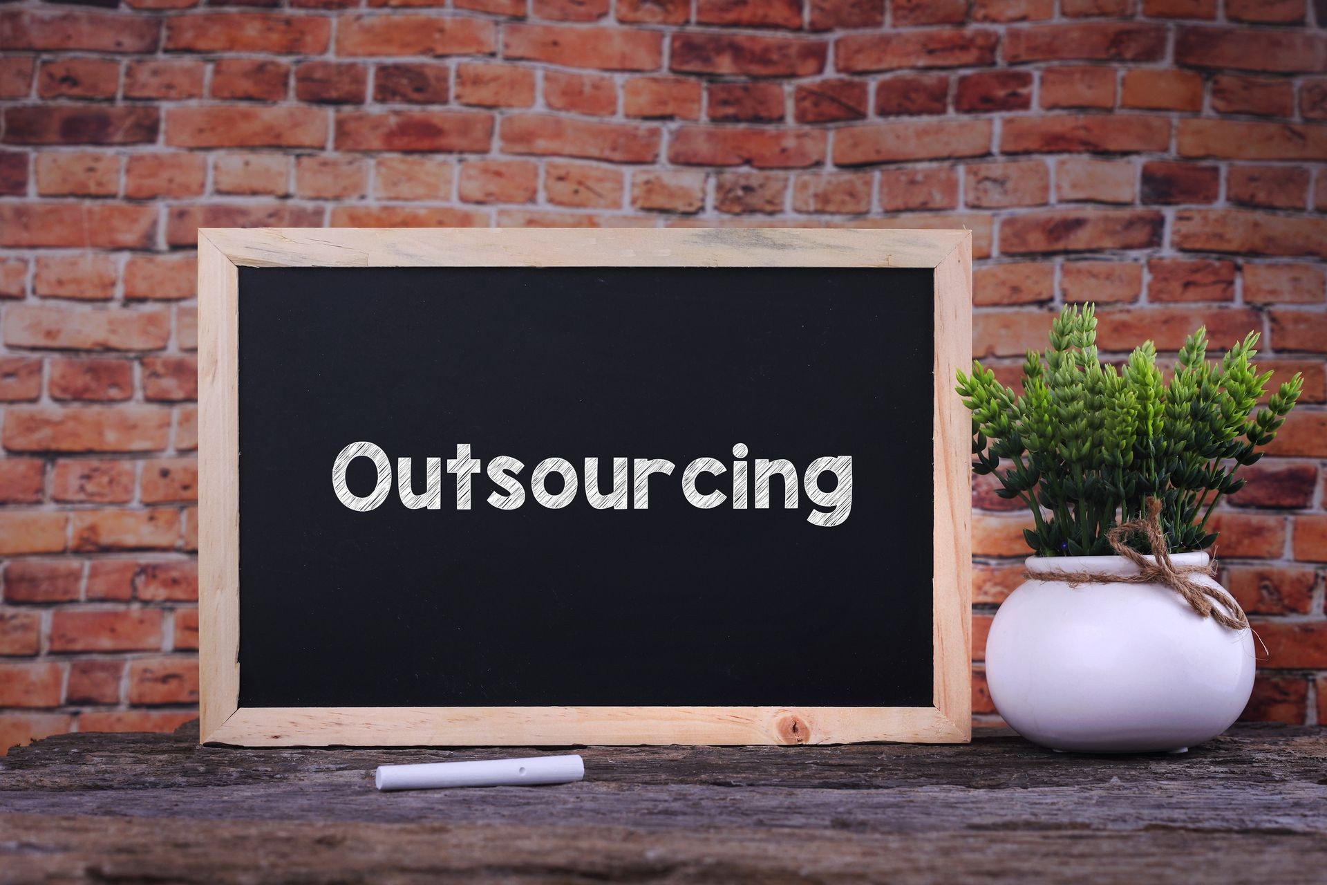 Outsourcing word on blackboard with green plant Outsourcing word on blackboard with green plant